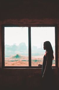 Side view of woman standing by window