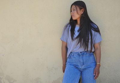 Beautiful young woman standing against wall