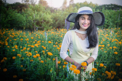 Portrait of smiling young woman wearing hat amidst flowers on field