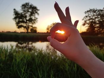 Close-up of hand gesturing against sunset