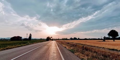 Empty road amidst field against sky during sunset