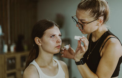 A young makeup artist applies a medicinal liquid under a girl s eyes.