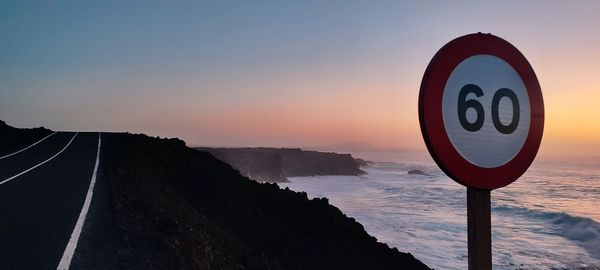 Scenic view of rocky volcanic coastline against sky during sunset with road sign in foreground 