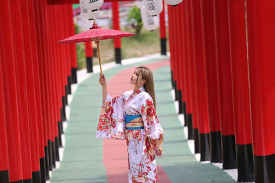 Woman holding umbrella standing against red wall