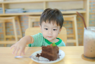 Cute boy reaching slice of cake in plate on table