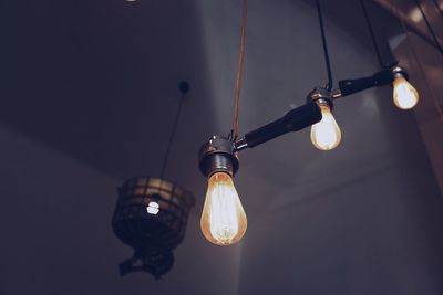 Low angle view of illuminated light bulbs hanging against ceiling