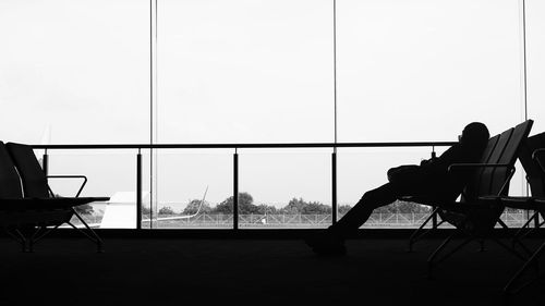 Man sitting on chair by window against clear sky