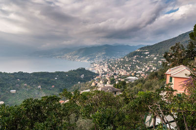 Buildings on tree mountain by sea against cloudy sky