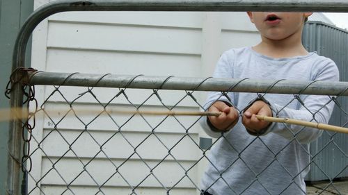 Midsection of boy playing with sticks by chainlink fence