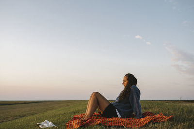 Woman sitting on field against sky