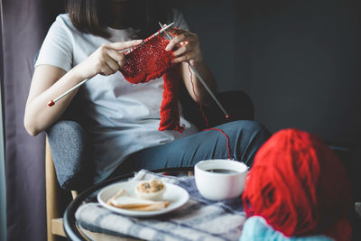 Midsection of woman knitting wool while having breakfast at home