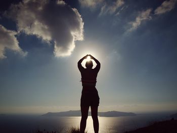Rear view of silhouette women gesturing standing on mountain against sky