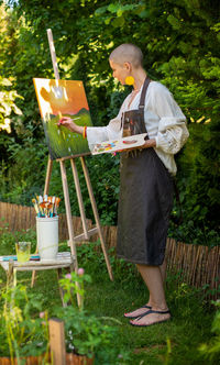 Young female artist working on her art canvas painting outdoors in her garden. art therapy.