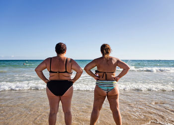 Rear view of young woman standing on beach against clear sky
