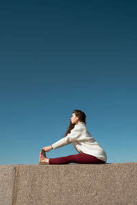 Woman sitting on wall against clear blue sky