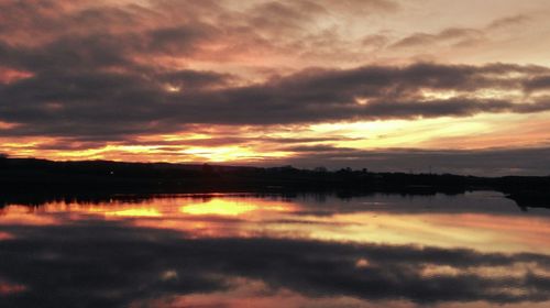 Scenic view of lake against dramatic sky during sunset