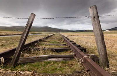 Rusty fence on field against sky