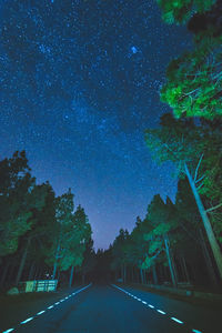 Empty road amidst trees against sky at night