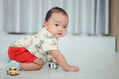 Portrait of cute baby boy playing with toy while sitting on floor at home