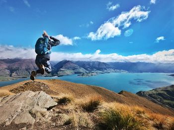 Full length of woman jumping on rock against sky