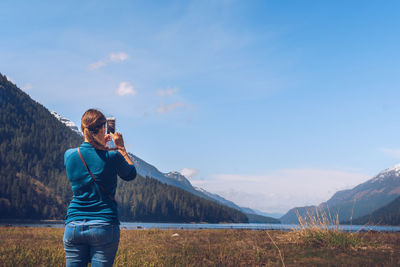 Full length of woman photographing landscape against sky