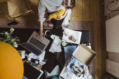 Directly above shot of businesswoman using laptop with sleeping son at home office