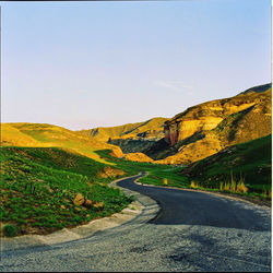 Road leading towards mountains against clear sky