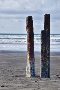 Wooden posts on beach against sky