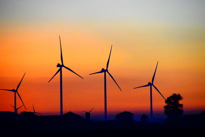 Silhouette wind turbines on field against sky during sunset