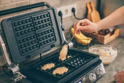Cropped hand of woman putting waffle batter in machinery