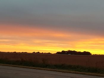 Road by landscape against sky during sunset