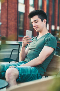 Smiling teenage boy using mobile phone in city