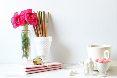 Office supplies with candies and flower vase on desk against white wall