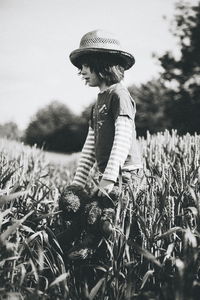 Boy holding teddy bear walking amidst wheat field against sky