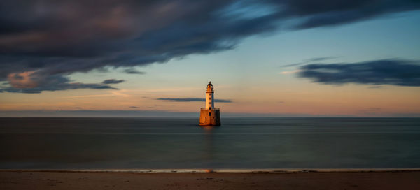 Lighthouse by sea against sky during sunset