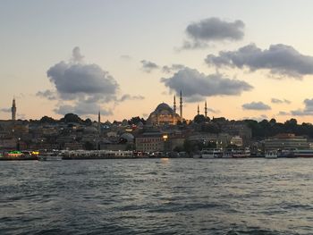 View of city at waterfront against cloudy sky