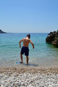 Full length of boy on rock at beach against clear sky