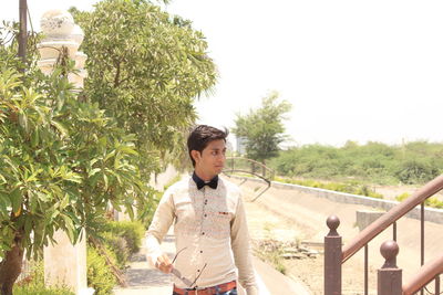 Young man standing by railing against clear sky