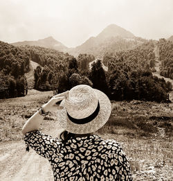 Rear view of woman holding onto straw hat looking at mountains