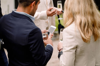 Businessman showing mobile phone to businesswoman while holding champagne flute