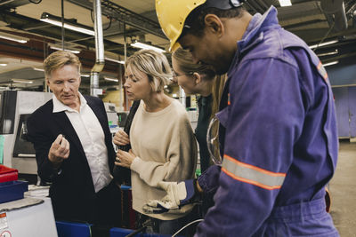 Male worker in protective workwear discussing with businessman and family in industry