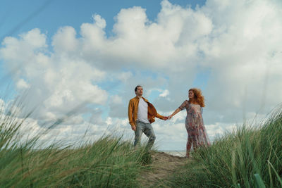 Couple standing on grass against sky