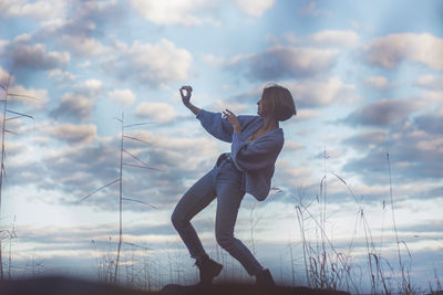 Young woman dancing on rock against cloudy sky