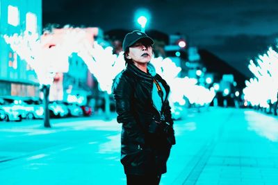 Portrait of man standing on illuminated street at night