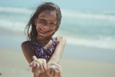 Portrait of smiling girl holding seashells while standing at beach during summer