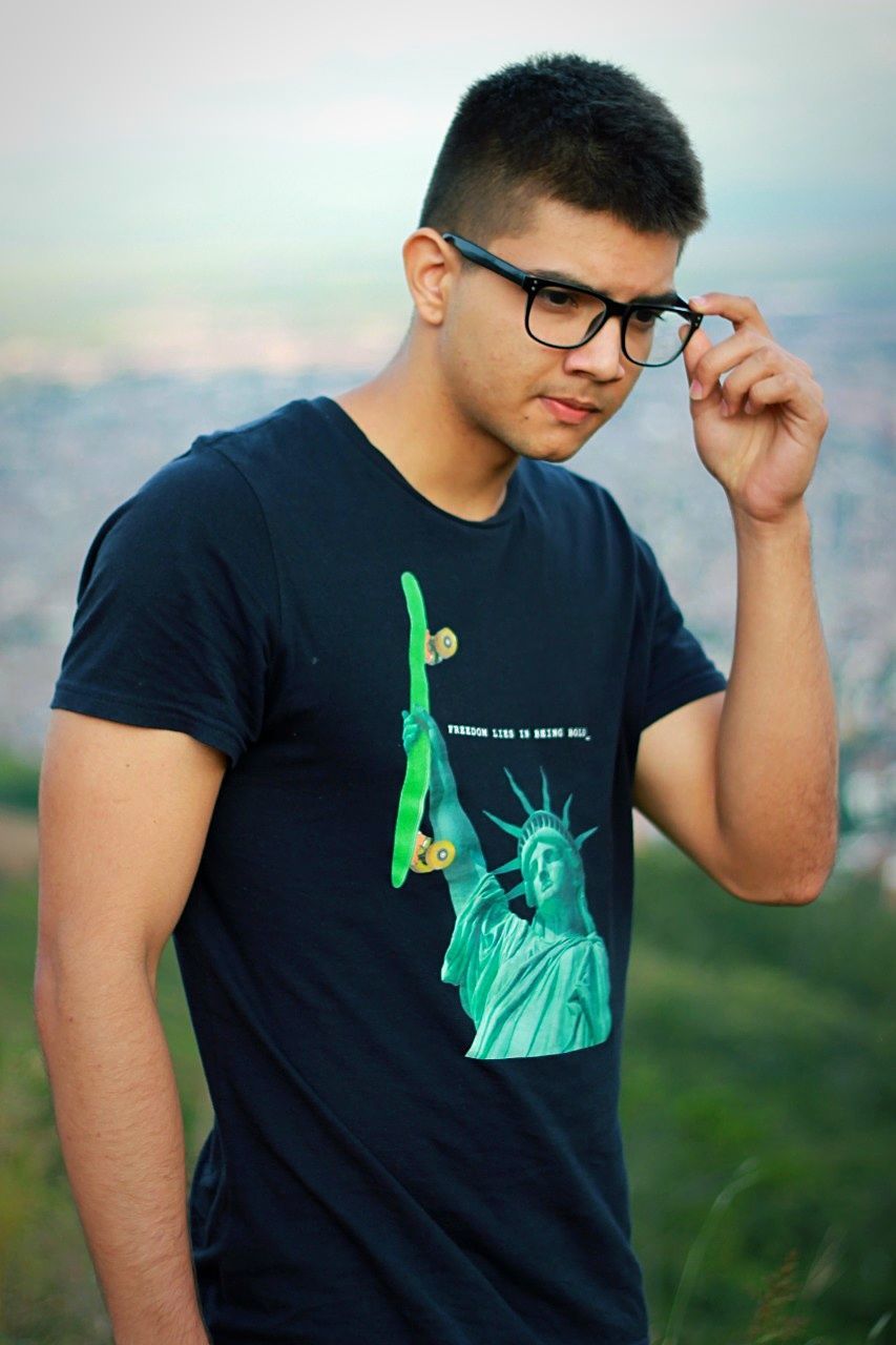 YOUNG MAN WITH EYEGLASSES STANDING AGAINST SEA