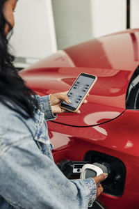 Woman using smart app on smart phone while charging electric car