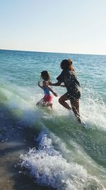 Children playing in sea against clear sky