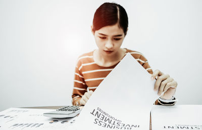 Young woman looking away while sitting on table against white background