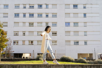 Female entrepreneur with arms outstretched walking in garden by building